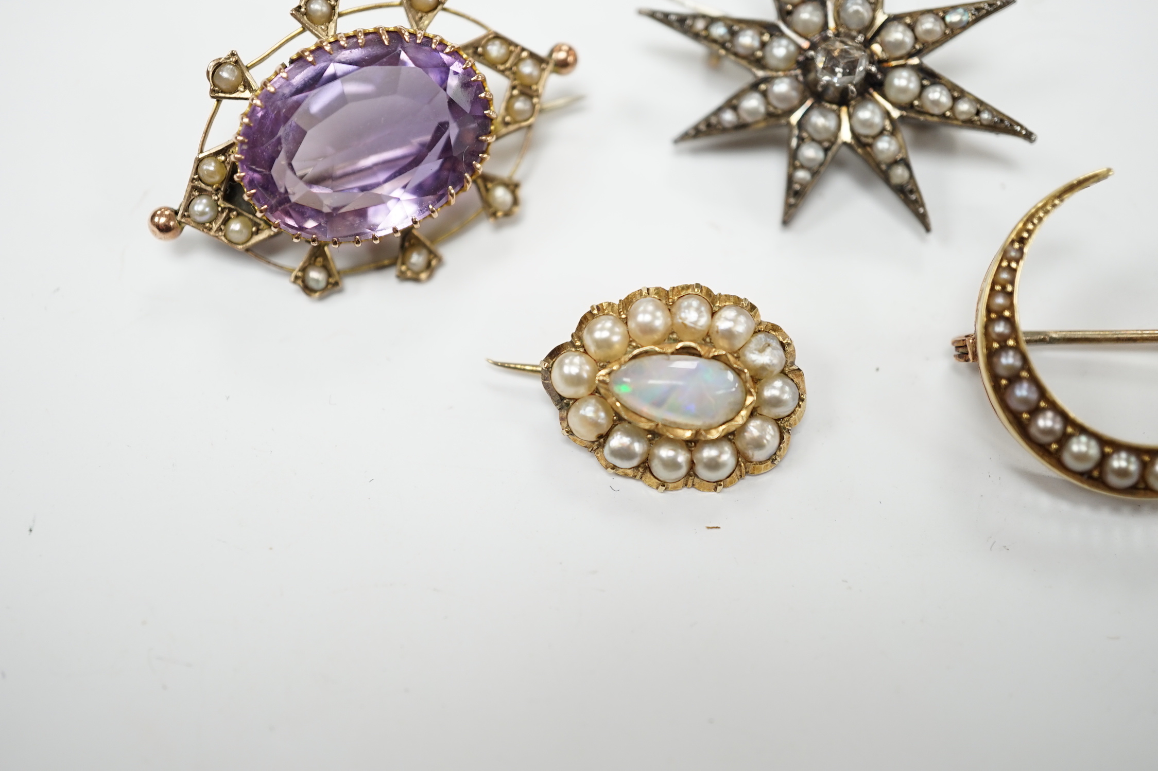 An early 20th century 9ct, amethyst and seed pearl set oval brooch, 33mm, a yellow metal and seed pearl set crescent brooch, a yellow metal, opal and split pearl set brooch and a rose cut diamond and split pearl set star